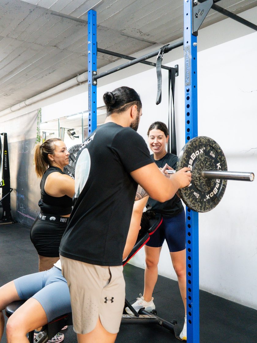 A coach guiding a member through a barbell squat at the rack