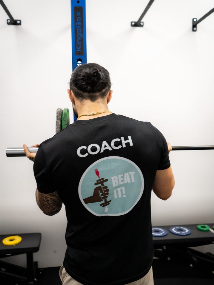 A coach seen from behind at the rack, COACH and the Beat It logo on the back of his black T-shirt