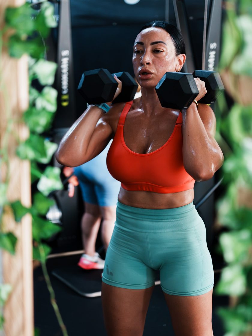 A member pressing two dumbbells at shoulder height during a class