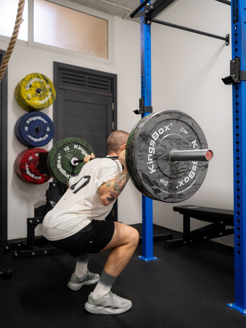 A man in a white T-shirt at the bottom of a heavy back squat in the rack